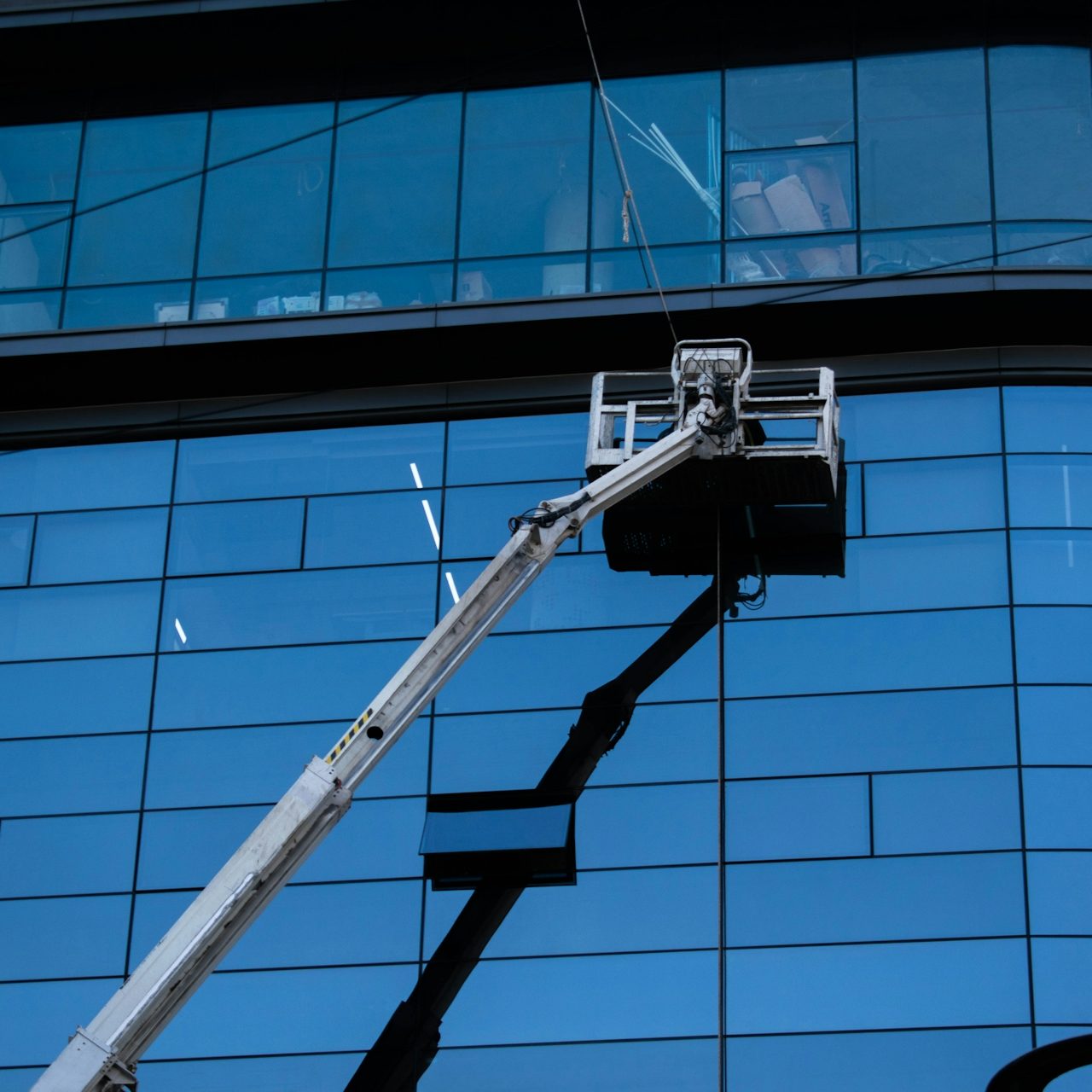 Ein Arbeitsbühne reinigt die Glasfassade eines modernen Gebäudes.