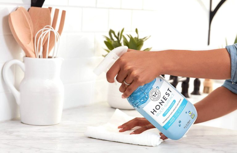 Eine Hand hält eine Sprayflasche mit Reinigungsmittel und wischt eine Oberfläche ab.